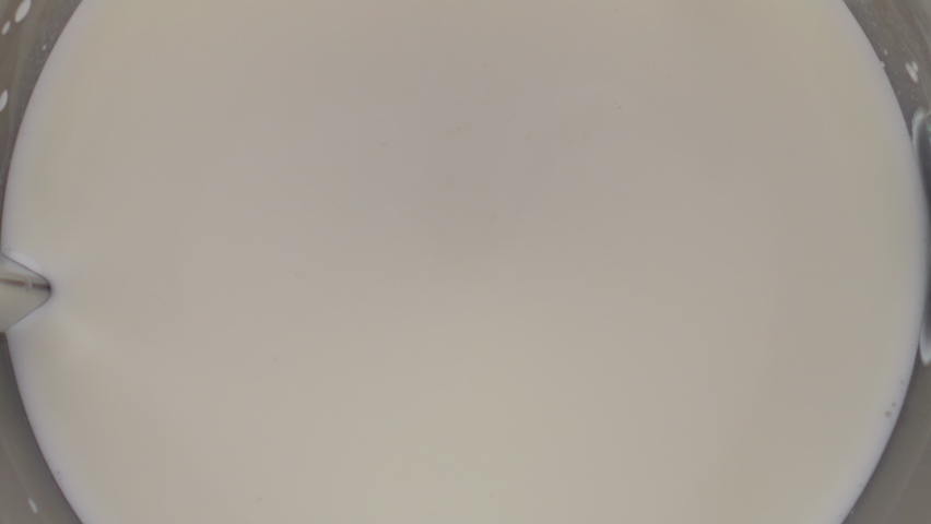 Fresh white milk splashing inside blender bowl close up. Organic dairy beverage swirling mixing in electric mixer super slow motion. Top view protein healthy ingredient for smoothie cocktail milkshake