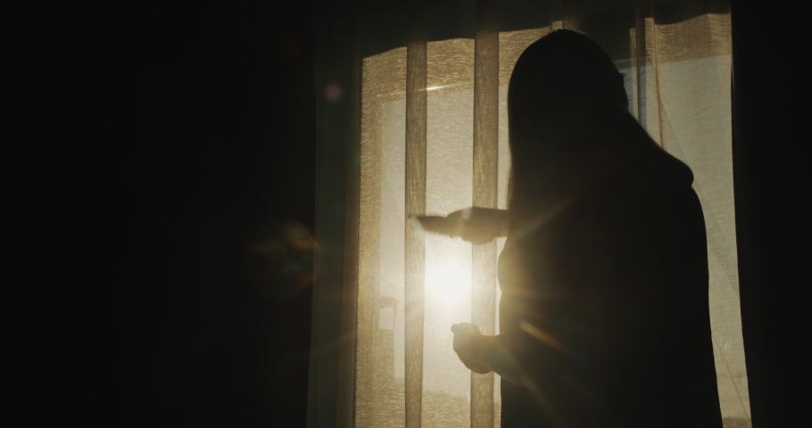 Silhouette of a middle-aged woman combing her hair at the window