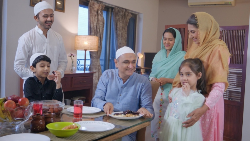 An Indian Asian ethnic Muslim happy family including parents,  grandparents, and kids or children are feeding each other dates while breaking a holy Ramadan fast during Eid al-Fitr or Ramzan festival. Royalty-Free Stock Footage #1095480943