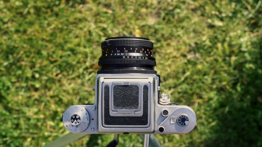 A photographer operating a vintage analog photo camera focusing ajusting taking pictures outside looking through a large square format viewfinder mechanical settings solid metal cogs garden background