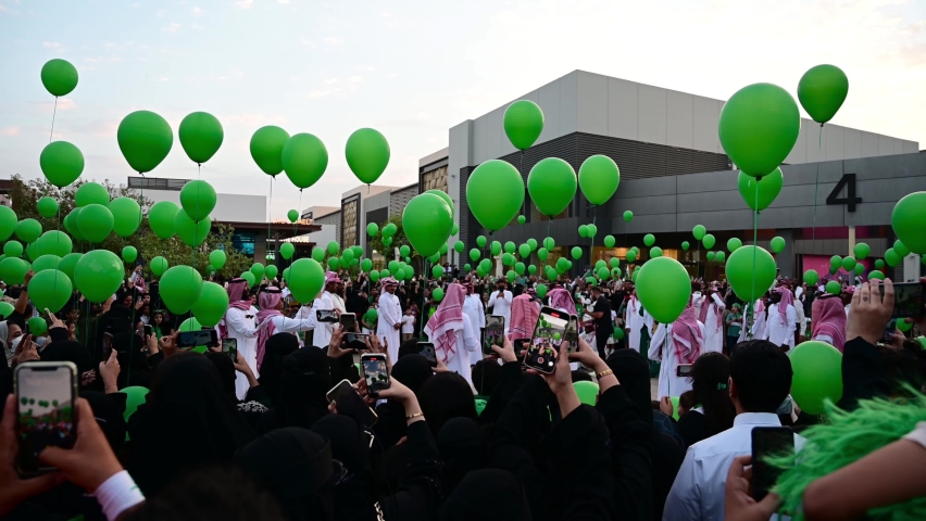 Riyadh, Saudi Arabia – September 23rd, 2020: Group of Saudi people celebrates the Saudi National Day by releasing green balloons to the sky while the Saudi National Song is played.