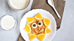 Funny sun face shape snack from pancake,orange on plate. Cute kids childrens baby's sweet dessert, healthy breakfast,lunch, food art with milk and sour cream on gray concrete background,top view.