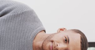 Vertical video half portrait of biracial man smiling to camera and laughing indoors with copy space. Health, happiness, inclusivity and lifestyle concept.