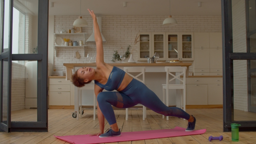 Active charming fit black woman in sportswear practicing world s greatest stretch exercise, working out hamstrings, glutes, hip flexors, quadriceps, calves, shoulders, pectorals, upper and lower back.