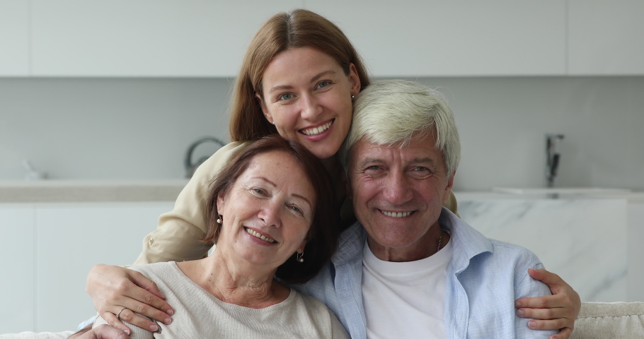 Optimistic beautiful multi generational family portrait concept. Loving millennial daughter hugs elderly mother and father smile pose look at camera, feel happy enjoy time together and warm relations Royalty-Free Stock Footage #1095495583