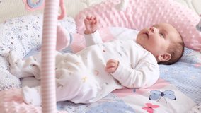 Cute newborn baby lying on a back and looking on toys. Infant baby laying on a play soft mat with toys. Childhood concept 