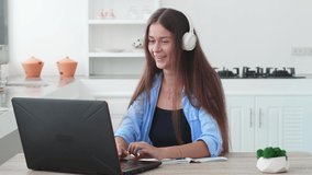 Confident young Caucasian woman, student or freelance entrepreneur, wearing wireless headphones, working remotely on laptop, talking with colleagues via video link. Online communication. Telecommute