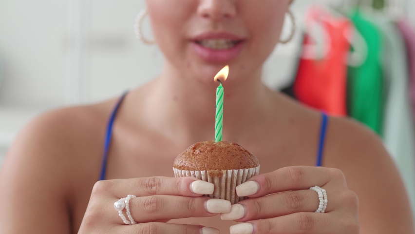 Selective focus on the baked sweet cupcake with a candle in the hands of a blurred beautiful woman, birthday girl blowing out the candle on her birthday cake and smiling broadly. Happy birthday to me