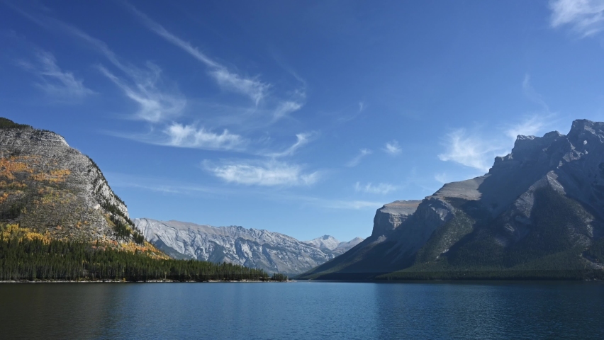 Large mountain lake with small waves surrounded by large mountains under a blue skies with wispy white clouds
