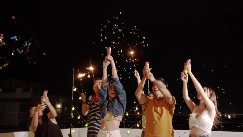 Group of young Asian friends lit light sparkler, sing and dance together at roof top on weekend celebration.