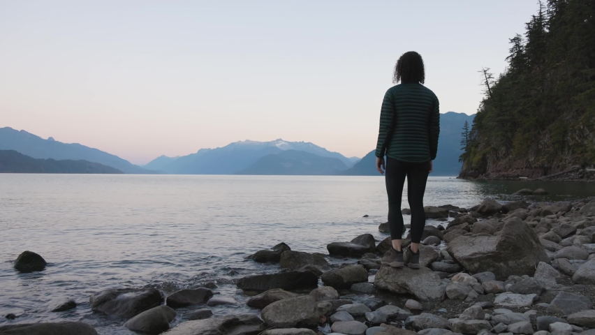 Adventure Travel Woman standing at Harrison Lake during Sunny Summer Morning Sunrise. Canadian Nature Landscape Background. Harrison Hot Springs, British Columbia, Canada. Slow Motion Cinematic