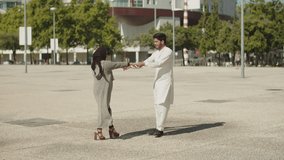 Romantic Muslim couple dancing together in street on sunny day. Young Arabic man and woman in traditional clothes holding hands, having fun outside. City background. Ethnicity, love concept. 