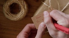 Man writing a gift tag with text FROM ME TO YOU on eco friendly wrapped gift box, close up view. - Powered by Shutterstock - Get 15% off with code: PIKWIZARD15