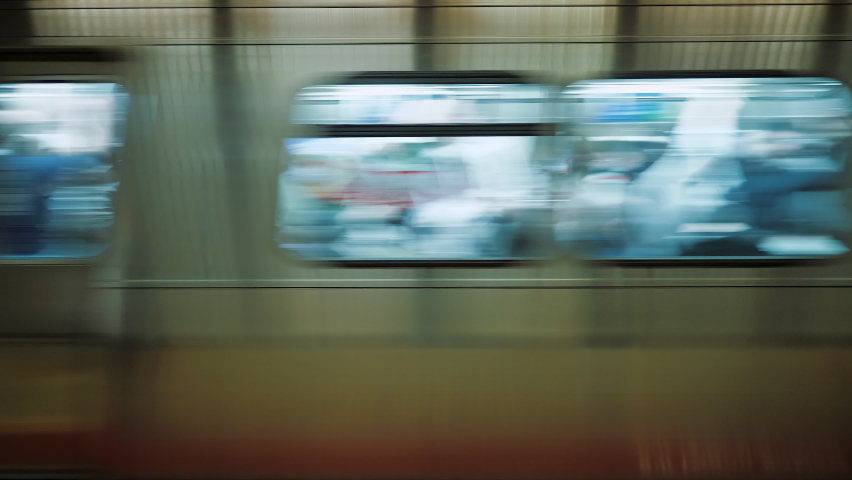 Subway train with people inside moving fast from metro station, close up. Windows of train passing at underground station