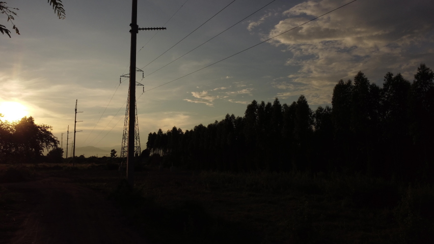 Aerial view of high voltage pylons and wires in the sky at sunset in the countryside. Drone footage of electric poles and wires at dusk.