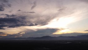 Aerial view of beautiful sky with clouds and sunlight during sunset. Time lapse of the clouds above the sky with the golden rays of the sun against the background of the silhouette of the mountain lan
