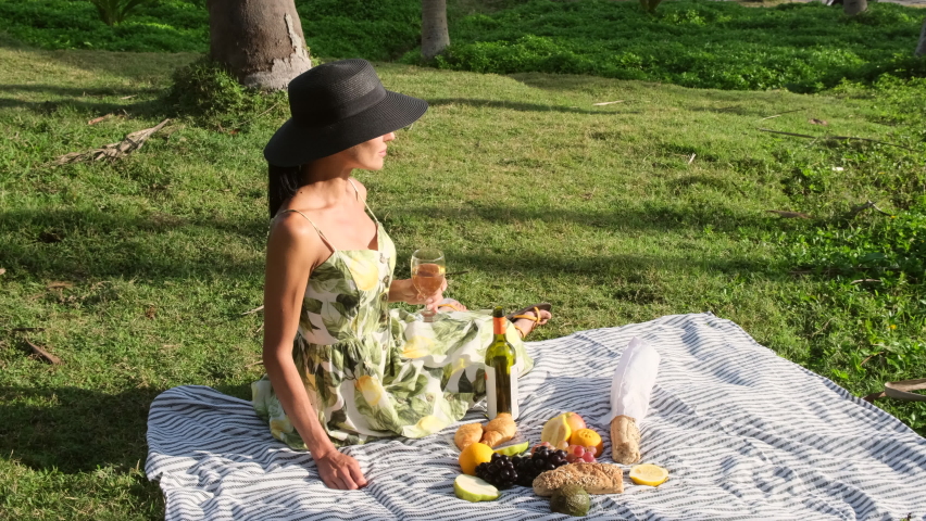 Happy caucasian woman in straw hat with curly hair enjoy picnic by the sea outdoors, eat croissant, look at the camera. Young woman having a picnic with sea view