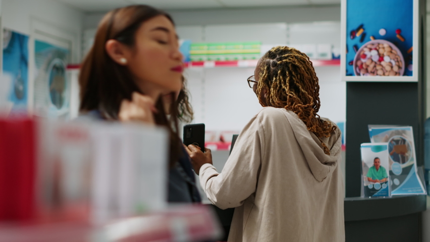 African american person asking pharmacist about prescription treatment in bottle of pills to buy from pharmacy shop. Medical worker serving woman with pharmaceutical products and medication.