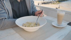 Man eating pasta carbonara with a fork in summer outdoor cafe near the beach. Tasty italian food for lunch or dinner. 4k video