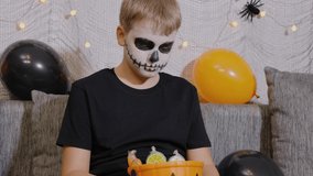 Boy in skeleton makeup holds a bucket of candy. The child celebrates Halloween - Powered by Shutterstock - Get 15% off with code: PIKWIZARD15