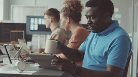 Young Black man using digital tablet while working in modern IT office with group of multiethnic colleagues coding and developing software - Powered by Shutterstock - Get 15% off with code: PIKWIZARD15