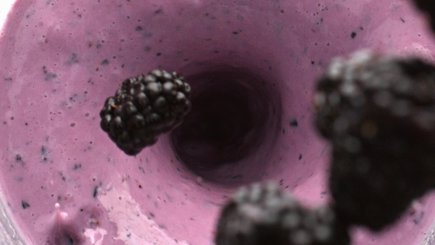 Bramble throwing smoothie blending inside bowl top view. Milk berries liquid whirlpool closeup. Creamy yoghurt beverage swirling in slow motion. Protein blackberry cocktail cooking mixing in container Royalty-Free Stock Footage #1095537681