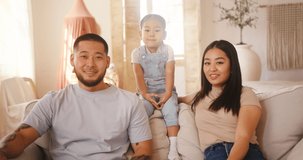 Asian family talks via videocalls with bestfriends. Father and mother sitting on couch in apartment with toddler daughter discuss future weekends