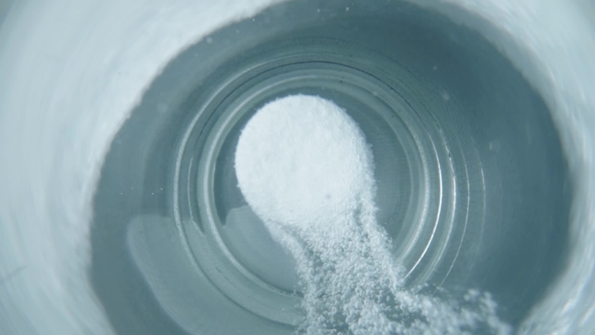 Macro shot of white round tablet of soluble aspirin bubbling in glass of water. Effervescent tablet of acetylsalicylic acid dissolves in water forming many hiss bubbles. Headache pill.