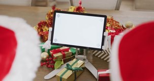 Video of couple in santa hats with gifts making christmas video call on tablet with copy space. Christmas, communication, tradition, celebration and inclusivity concept.