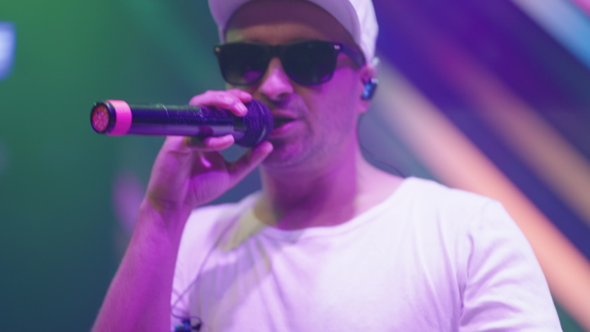 portarit of cool rapper or singer on stage during gig, man with black glasses and cap are rapping and singing