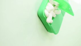 Vertical video of hand taking a pill from some pills in a green pillbox on green background