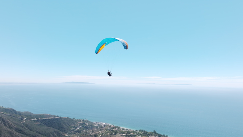 Epic closeup shot of two paragliders waving in drone camera while flying in skies, above cinematic teal ocean coast. Woman with instructor flies with paraglide 4k. Aerial drone footage above Malibu US Royalty-Free Stock Footage #1095554527