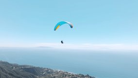 Epic closeup shot of two paragliders waving in drone camera while flying in skies, above cinematic teal ocean coast. Woman with instructor flies with paraglide 4k. Aerial drone footage above Malibu US