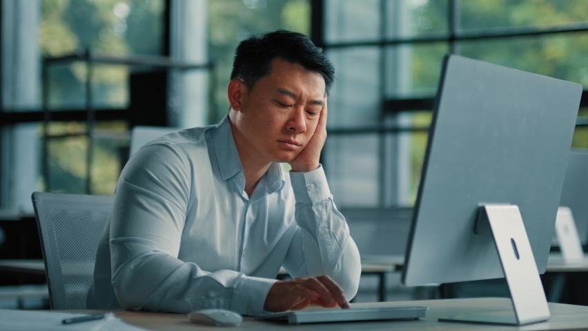Bored lazy asian worker businessman korean japanese man exhausted weary male sit in office asleep tired from boring online work at computer develop business project unwell feeling lack of motivation | Shutterstock HD Video #1095554947
