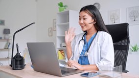 Young Asian female doctor greeting patient looking at laptop screen during video conference call for online consultation. Woman therapist or pediatrician working on internet over world concept