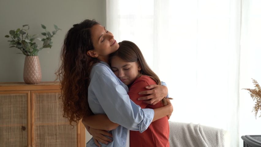 Friendly European woman with daughter at moment of congratulations on holiday or birthday stand in home interior. Happy teenage girl hugging mother after long separation or leaving for children's camp Royalty-Free Stock Footage #1095566801