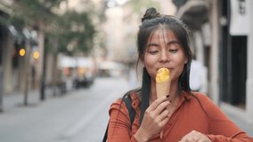 Asian woman smiling while eating a fresh ice cream cone outdoors in the street.