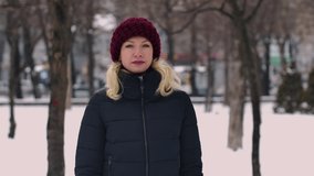Woman in a winter snowy park holding a smartphone and talking on a video call. The girl greets the interlocutor, shows a thumb up gesture, sends an air kiss and waves her hand. Close up. Slow motion.