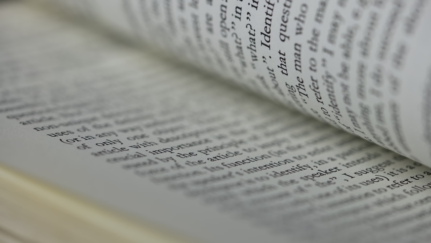 Open book close up. Macro shot of flipping white pages of a book with english text, side view. Part of the text is blurry. Slow motion. Royalty-Free Stock Footage #1095574427