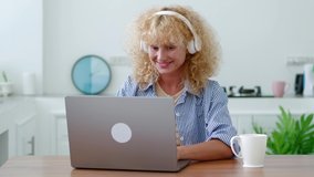 Inspired young Caucasian curly-haired woman in audio headsets, telecommuting, working remotely on laptop, typing text on keyboard, planning projects. Online business, freelance people, copywriter - Powered by Shutterstock - Get 15% off with code: PIKWIZARD15
