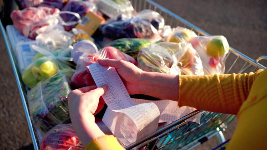 Worried woman checks a paper receipt after grocery shopping at a supermarket. Covid-19 global economy financial crisis concept, money saving. Food and grocery shopping