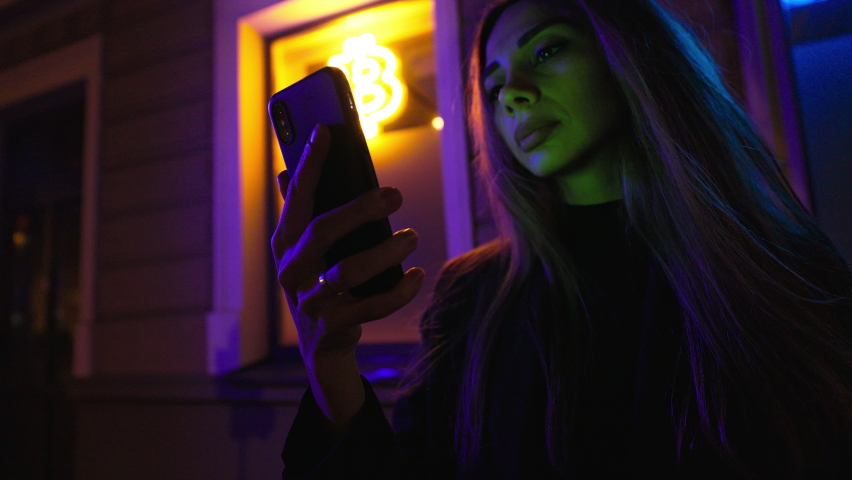 Focus on phone: Female crypto investor smiles and uses her smartphone to happily sell cryptocurrency