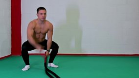 Nice real time footage of a handsome muscular young man using battle ropes for exercise in a gym. It is focused on performing the exercise, motivational video, copy space