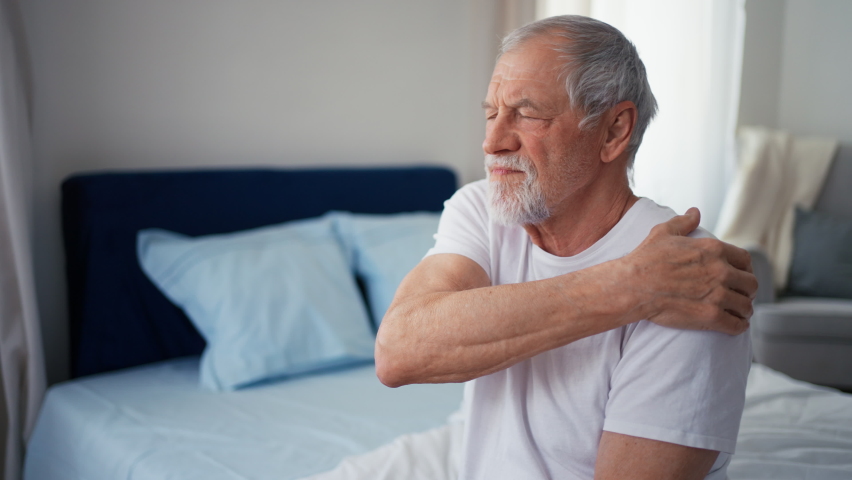 Senior man having shoulder pain, sitting in pyjama on his bed. Royalty-Free Stock Footage #1095582929