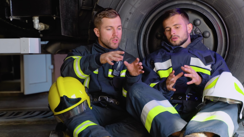 Two tired firefighters are sitting near a fire truck after a fire