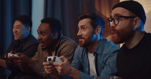 Men friends having fun playing video games and competing. Group of men isng joysticks sitting in living room and cheering each other