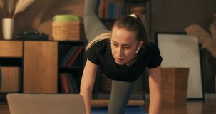 Sports woman training in front of laptop, living room interior. Healthy young woman in sportswear, exercising at home, watching fitness classes online.