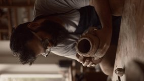  Vertical video, bearded man in glasses potter is concentrating on sculpting a jug from clay in a pottery workshop, hobby, making a cup from clay, handmade - Powered by Shutterstock - Get 15% off with code: PIKWIZARD15