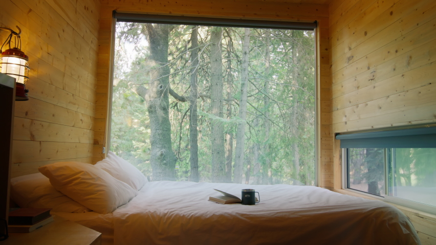 Modern Tiny House Interior In Forest, dolly shot on RED camera. Copy or text space with beautiful green spruce forest on motion background on sunny summer day.Pine trees seen through large window wall Royalty-Free Stock Footage #1095749149