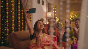 Happy smiling Hindu ethnic Indian family members in traditional attire posing to take or click a selfie picture or photo together using a mobile phone or smartphone during Diwali festival season.	